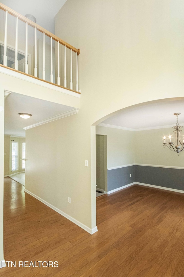 spare room featuring an inviting chandelier, wood finished floors, ornamental molding, and arched walkways