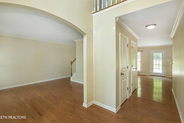 corridor featuring stairs, wood finished floors, ornamental molding, arched walkways, and baseboards