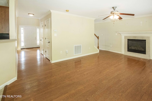 unfurnished living room featuring wood finished floors, a ceiling fan, visible vents, ornamental molding, and stairs