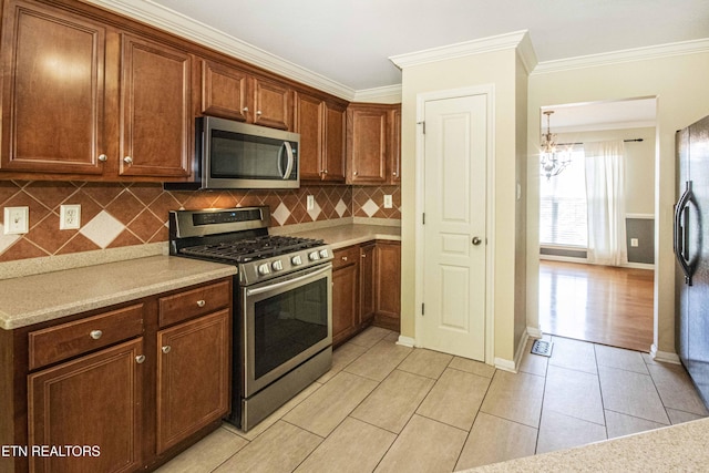 kitchen with ornamental molding, an inviting chandelier, light countertops, tasteful backsplash, and appliances with stainless steel finishes