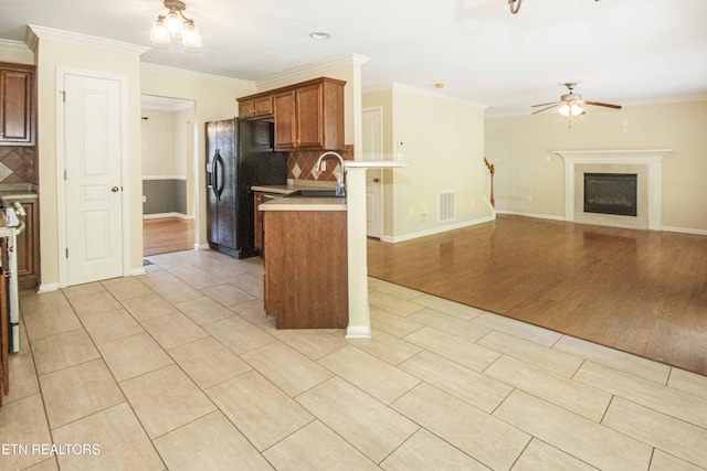 kitchen with black refrigerator with ice dispenser, tasteful backsplash, brown cabinetry, ceiling fan, and a fireplace