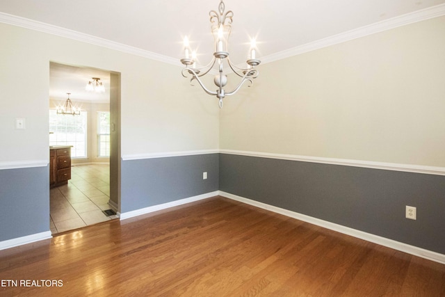 empty room featuring a chandelier, ornamental molding, baseboards, and wood finished floors