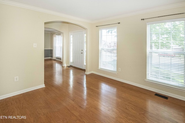 foyer entrance featuring crown molding, arched walkways, baseboards, and visible vents