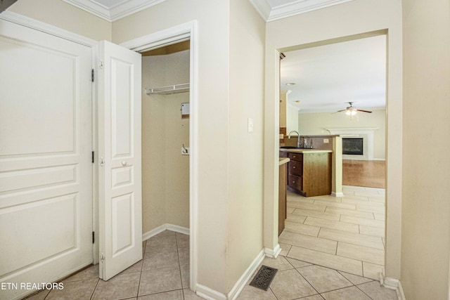 corridor with a sink, ornamental molding, visible vents, light tile patterned floors, and baseboards