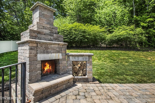 view of patio with a warm lit fireplace and fence