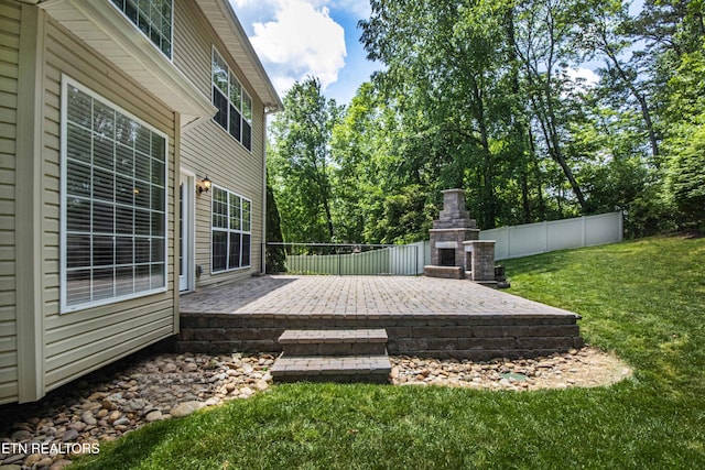 wooden deck featuring a patio area, an outdoor stone fireplace, fence, and a lawn