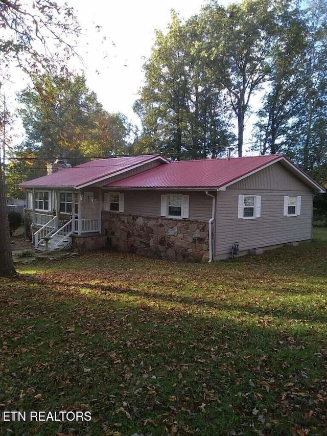 back of property with a yard, metal roof, and stone siding