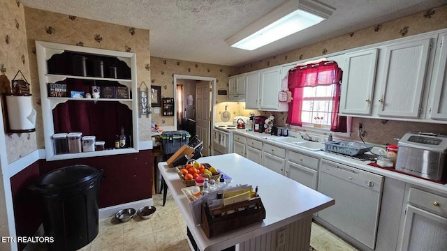 kitchen with white appliances, light countertops, a textured ceiling, white cabinetry, and wallpapered walls