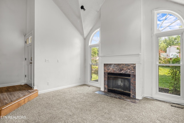 unfurnished living room with baseboards, a high end fireplace, carpet, and high vaulted ceiling