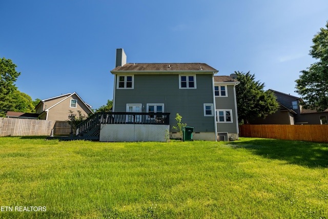 back of property featuring fence, a wooden deck, a chimney, and a yard