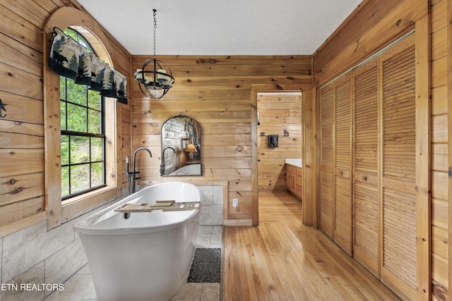 bathroom featuring wooden walls, a chandelier, wood-type flooring, and a freestanding bath