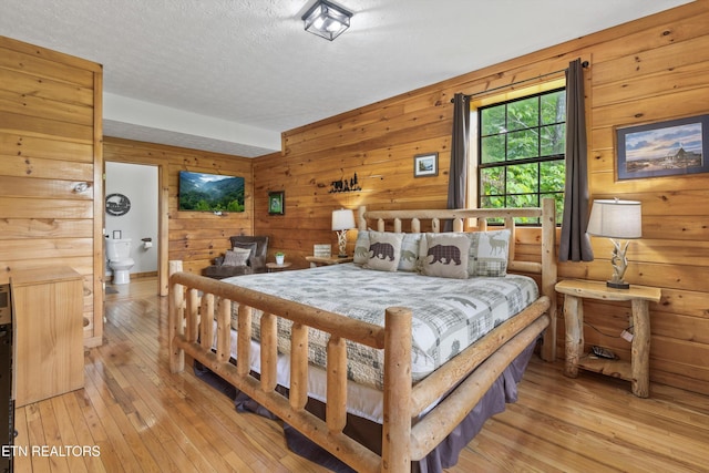 bedroom with light wood-style floors, wooden walls, and a textured ceiling