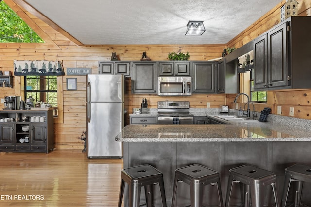 kitchen with wooden walls, a sink, stainless steel appliances, a peninsula, and light wood-type flooring