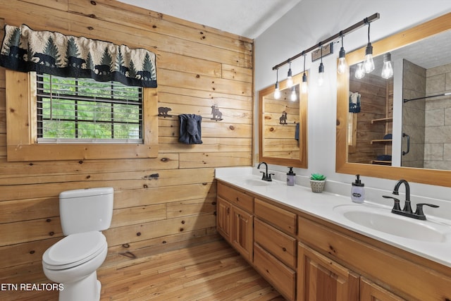full bath featuring double vanity, a stall shower, wood walls, a sink, and toilet