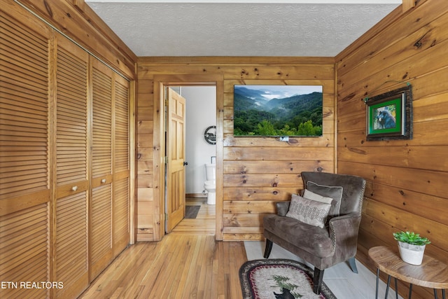 living area featuring wooden walls, a textured ceiling, and light wood-style floors