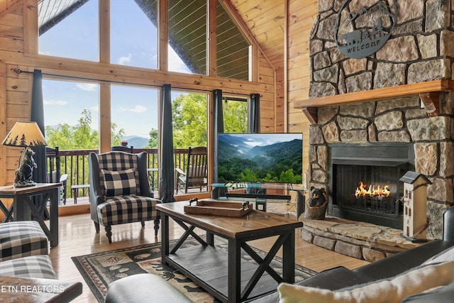 living area featuring wooden walls, high vaulted ceiling, a stone fireplace, wood ceiling, and hardwood / wood-style flooring