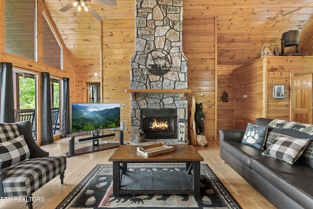 living area with ceiling fan, a stone fireplace, vaulted ceiling, wooden walls, and hardwood / wood-style floors