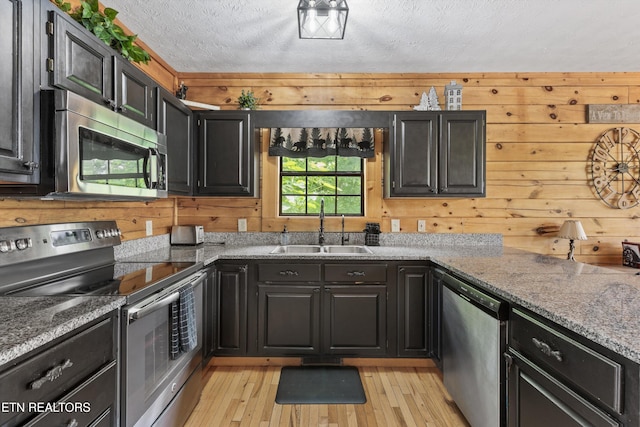 kitchen with wooden walls, a textured ceiling, a sink, light wood finished floors, and stainless steel appliances