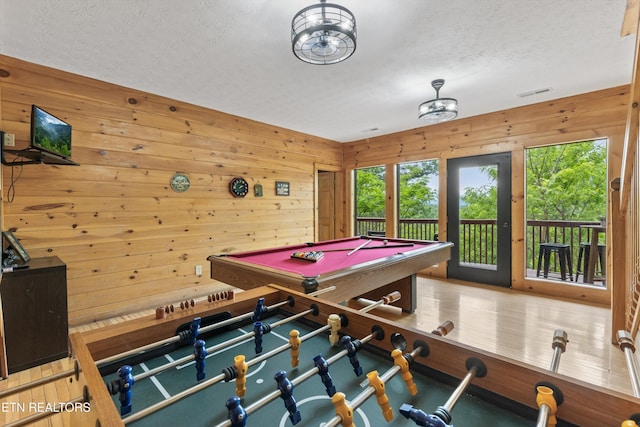 recreation room featuring visible vents, wood walls, a textured ceiling, and a healthy amount of sunlight