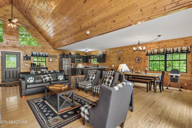 living room with wooden walls, plenty of natural light, light wood-type flooring, and an inviting chandelier
