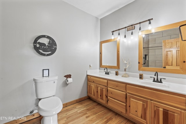 bathroom featuring a sink, double vanity, toilet, and wood finished floors