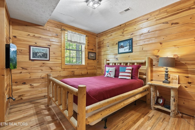 bedroom with visible vents, a textured ceiling, wooden walls, and hardwood / wood-style flooring