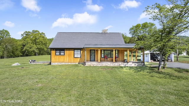 back of house featuring a yard, a porch, a chimney, and aphalt driveway