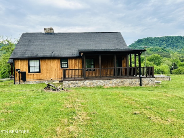 back of property featuring roof with shingles, a chimney, and a lawn