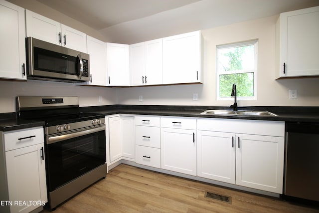 kitchen with dark countertops, appliances with stainless steel finishes, a sink, light wood-style floors, and white cabinetry