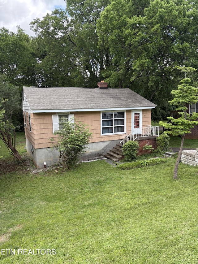 view of front facade with roof with shingles and a front yard