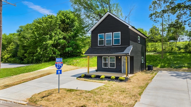view of front facade featuring covered porch, concrete driveway, a shingled roof, central AC unit, and a front lawn