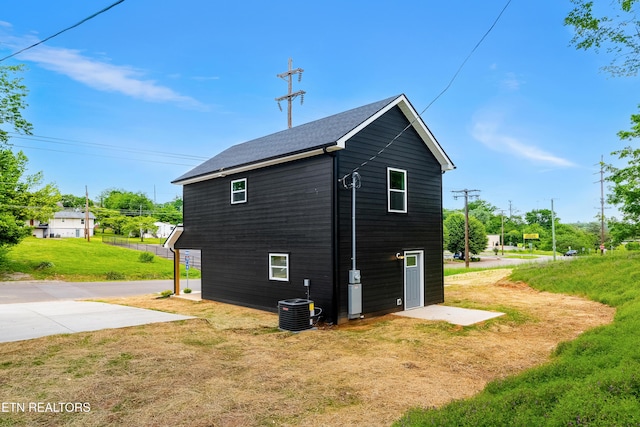 view of side of property featuring a yard, cooling unit, and roof with shingles