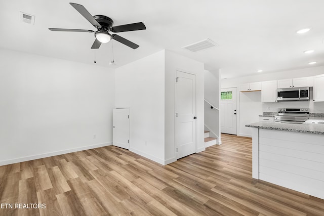interior space featuring white cabinetry, visible vents, light wood-type flooring, appliances with stainless steel finishes, and light stone counters