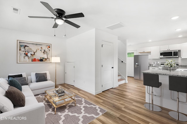 living room featuring stairway, ceiling fan, light wood-type flooring, and visible vents