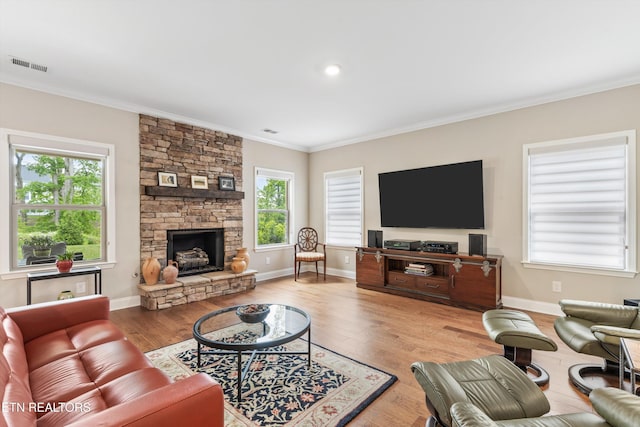 living room featuring baseboards, a stone fireplace, visible vents, crown molding, and wood finished floors
