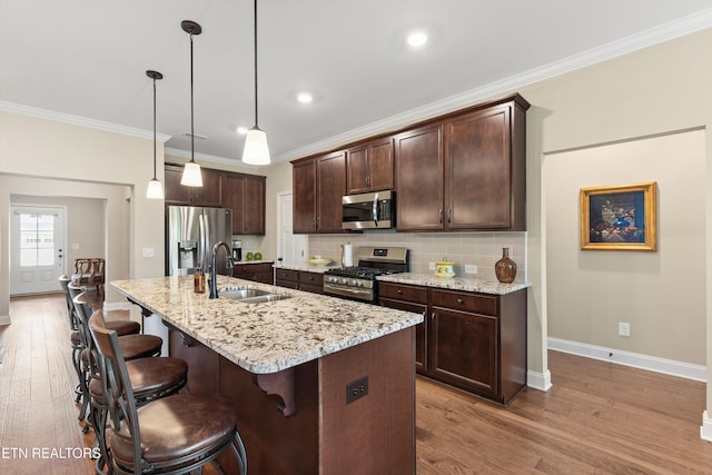 kitchen featuring a sink, stainless steel appliances, wood finished floors, baseboards, and dark brown cabinets