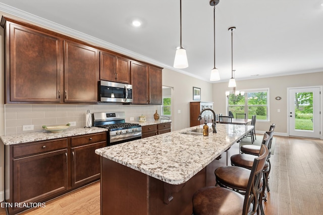 kitchen with light wood finished floors, a sink, a kitchen bar, decorative backsplash, and stainless steel appliances