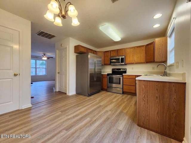 kitchen featuring visible vents, brown cabinetry, light wood-type flooring, a sink, and appliances with stainless steel finishes