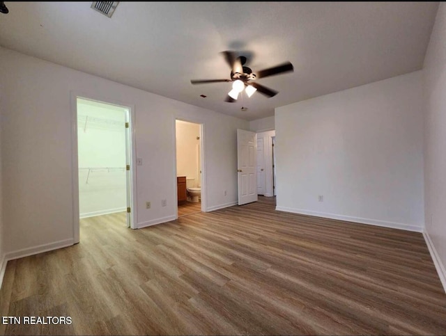 unfurnished bedroom with a walk in closet, baseboards, wood finished floors, ensuite bathroom, and visible vents
