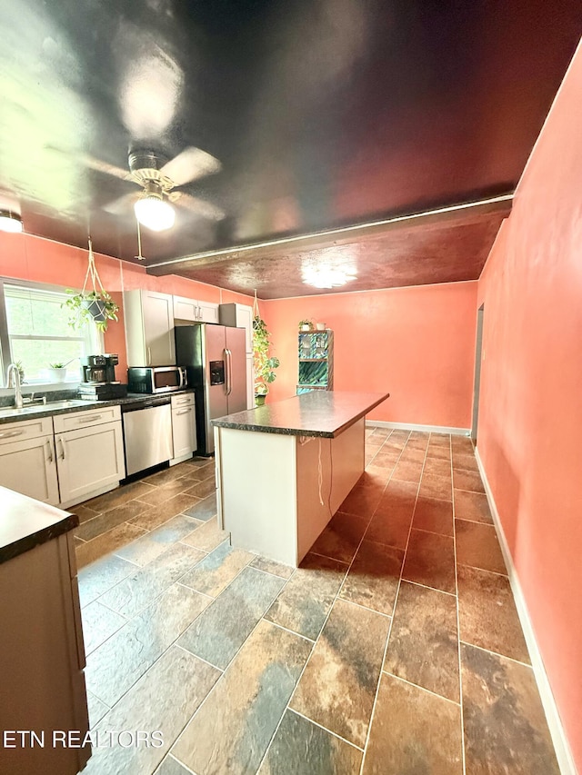 kitchen with a ceiling fan, appliances with stainless steel finishes, a sink, baseboards, and stone tile floors