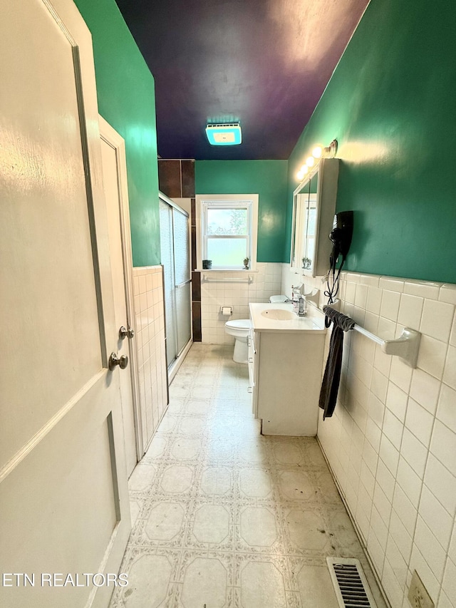 bathroom with vanity, toilet, a wainscoted wall, tile walls, and a stall shower