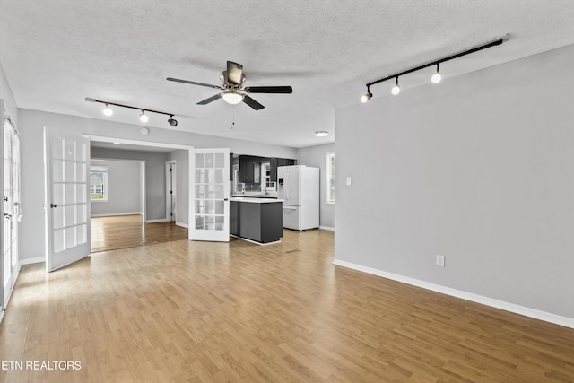 unfurnished living room featuring rail lighting, a textured ceiling, french doors, and ceiling fan