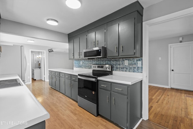 kitchen with light countertops, appliances with stainless steel finishes, decorative backsplash, and light wood-style floors