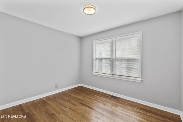 unfurnished room with wood finished floors, visible vents, and baseboards