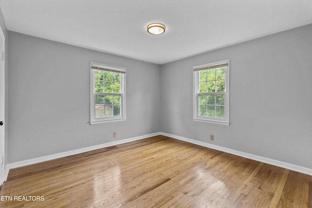 unfurnished room featuring baseboards, a wealth of natural light, and wood finished floors