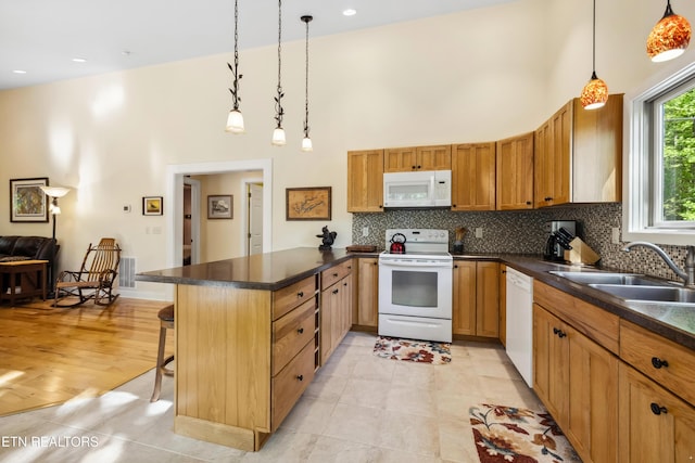 kitchen featuring white appliances, a high ceiling, a peninsula, a sink, and dark countertops