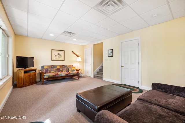 living area featuring a drop ceiling, carpet flooring, baseboards, and stairs