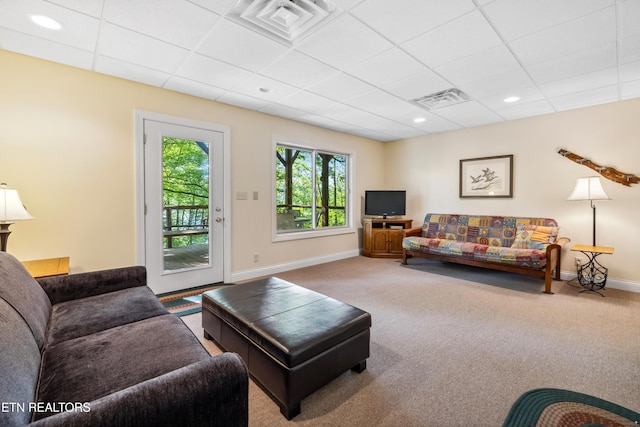 carpeted living area featuring a drop ceiling and baseboards