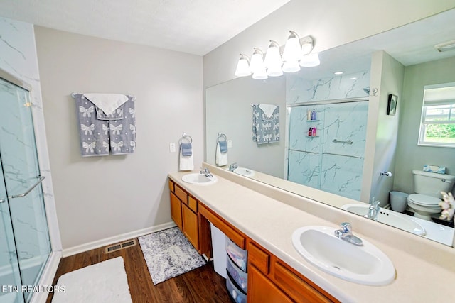 bathroom with wood finished floors, a marble finish shower, toilet, double vanity, and baseboards