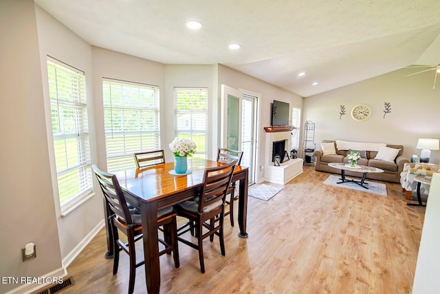 dining area with light wood-style floors, baseboards, a brick fireplace, ceiling fan, and lofted ceiling